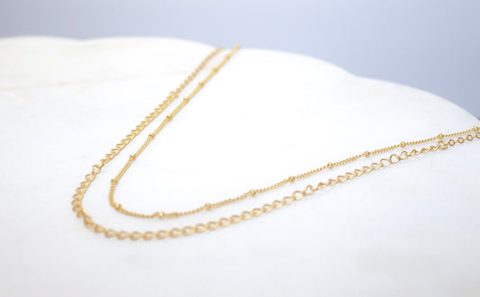 Gold chain necklace on a white cushion with a light gray background