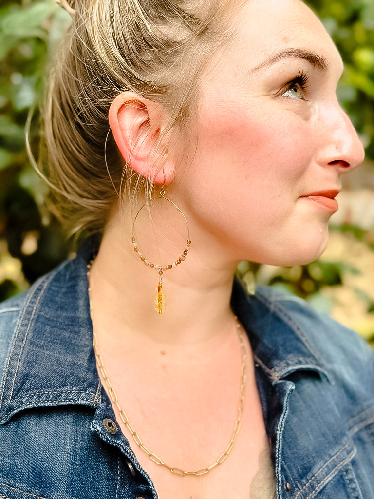 Woman wearing a gold necklace with a yellow pendant outdoors